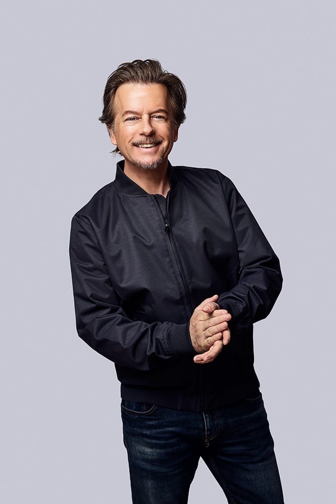 actor, David Spade, holding his hands together and smiling for picture